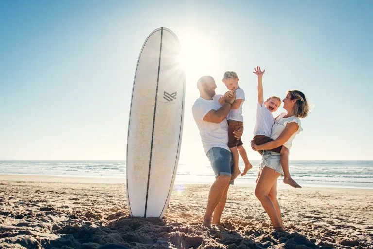 Famille sur une plage avec le soleil le ciel bleu et une planche de surf