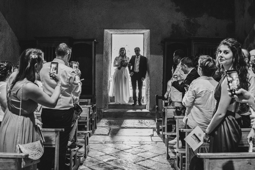 photo en noir et blanc de la mariée qui entre dans l'église au bras de son papa