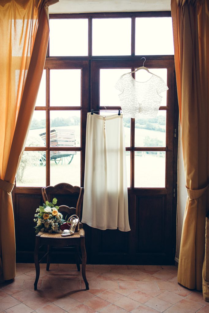 robe suspendue en toute élégance et transparence dans la lumière avec son bouquet jaune et blanc et ses talons louboutin pour son mariage au relais de porthos à Ogenne-Camptort