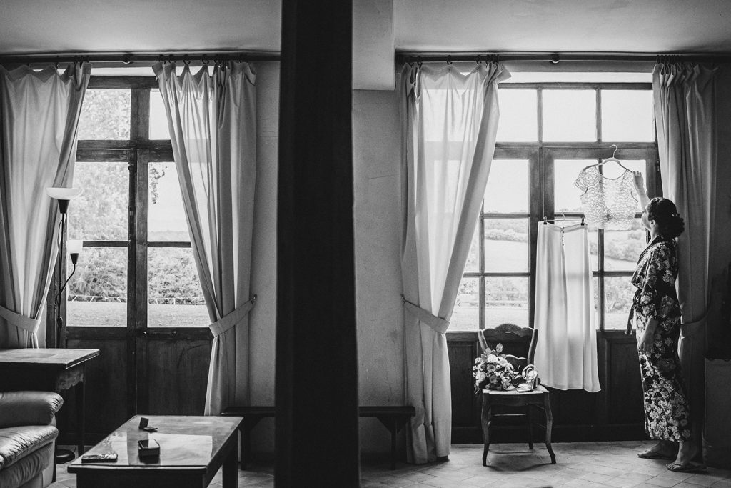 La mariée récupère sa robe suspendue dans une magnifique lumière lors de ses préparatifs de son mariage au relais de porthos à Ogenne-Camptort