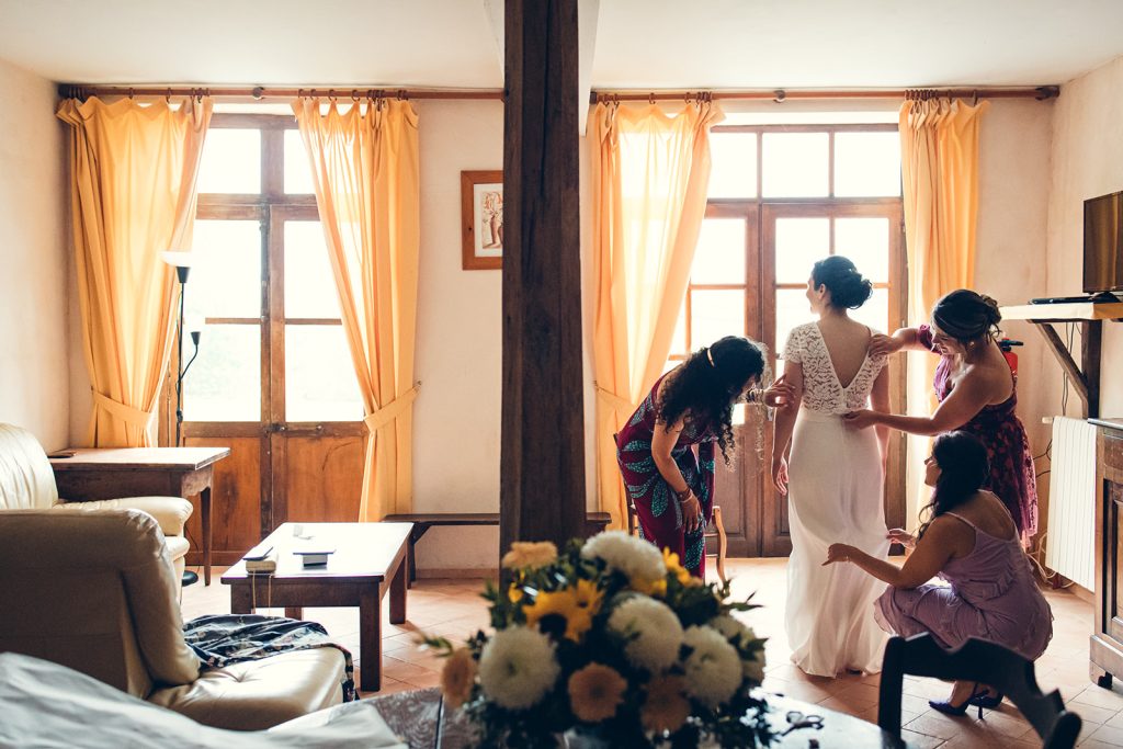 La mariée se fait habiller par ses demoiselles d'honneur dans une magnifique lumière au relais de porthos à Ogenne-Camptort