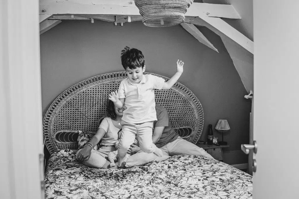 Le grand frère saute sur le lit des parents lors d'une séance naissance à domicile à nay