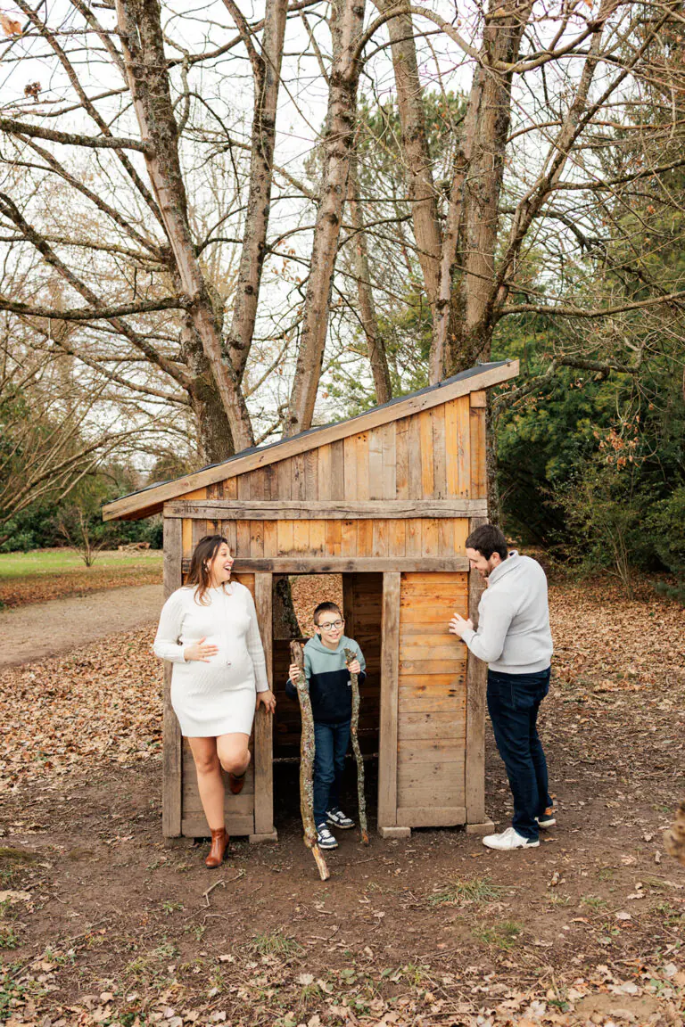 la famille joue devant une cabane en bois et la maman est enceinte du deuxième enfant séance grossesse pau
