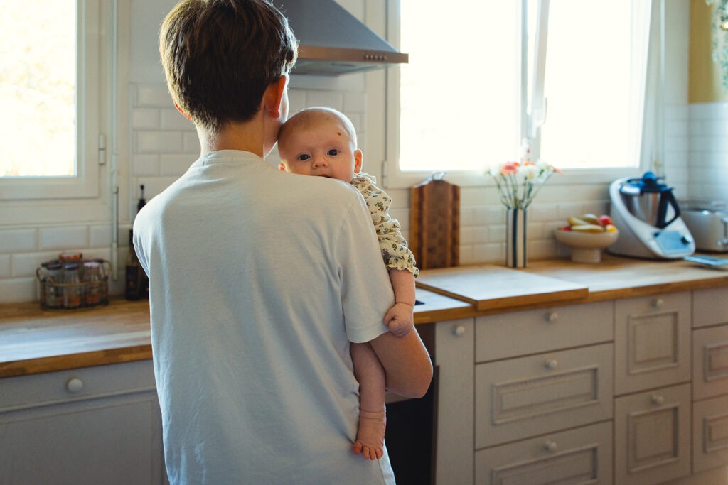 un grand frère qui porte sa petite soeur dans la cuisine de la maison