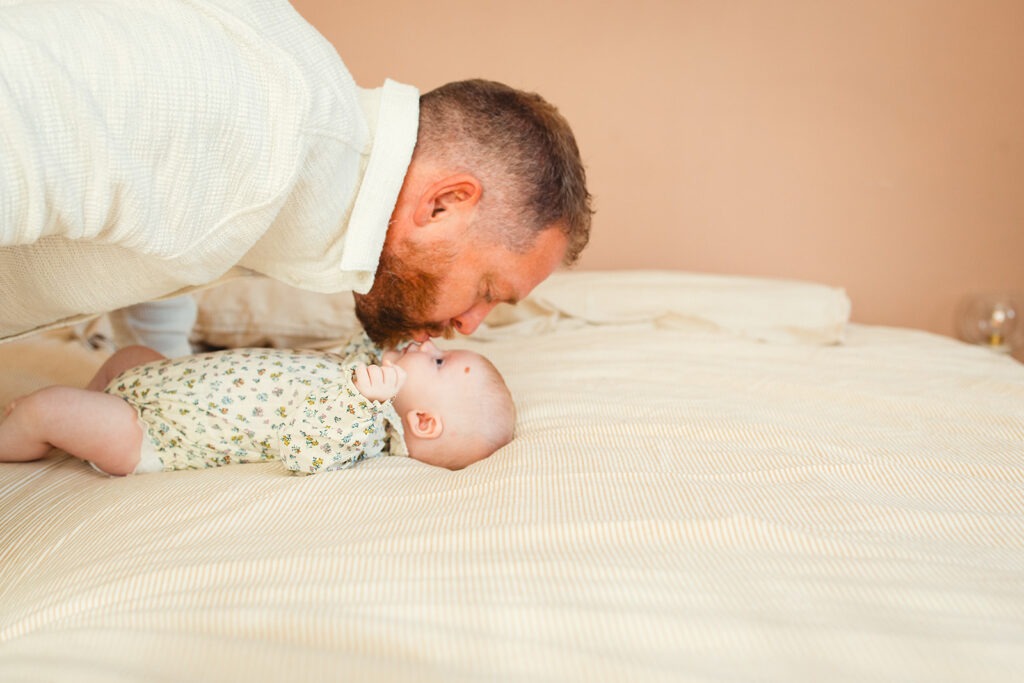 un papa fait un bisou à son bébé sur le lit