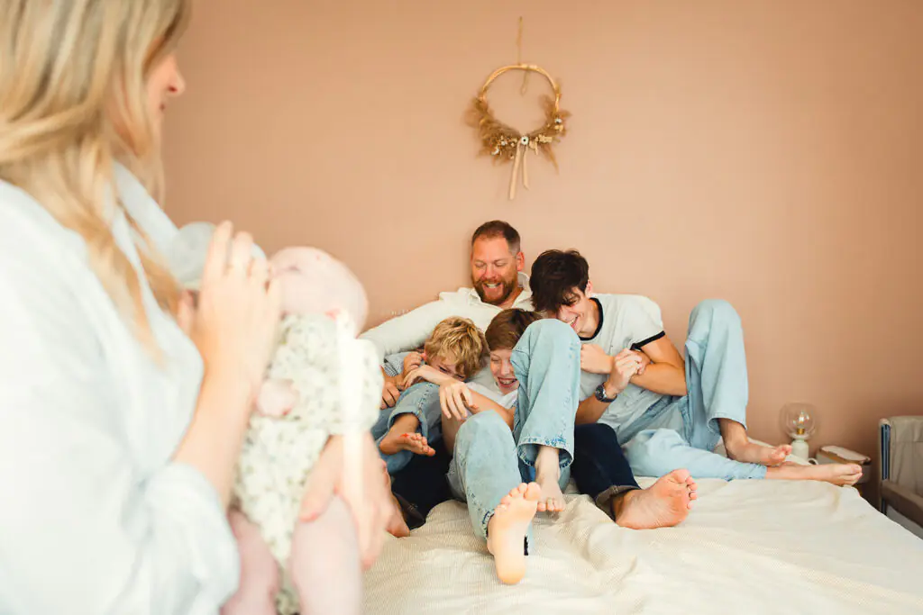 le papa joue avec les grands frères pendant que la maman berce son bébé